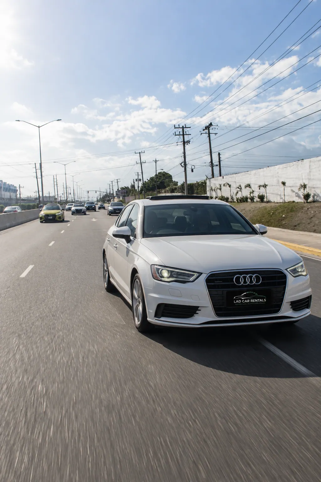 White Audi A3 with an LAD Car Rentals plate driving down a sunny highway